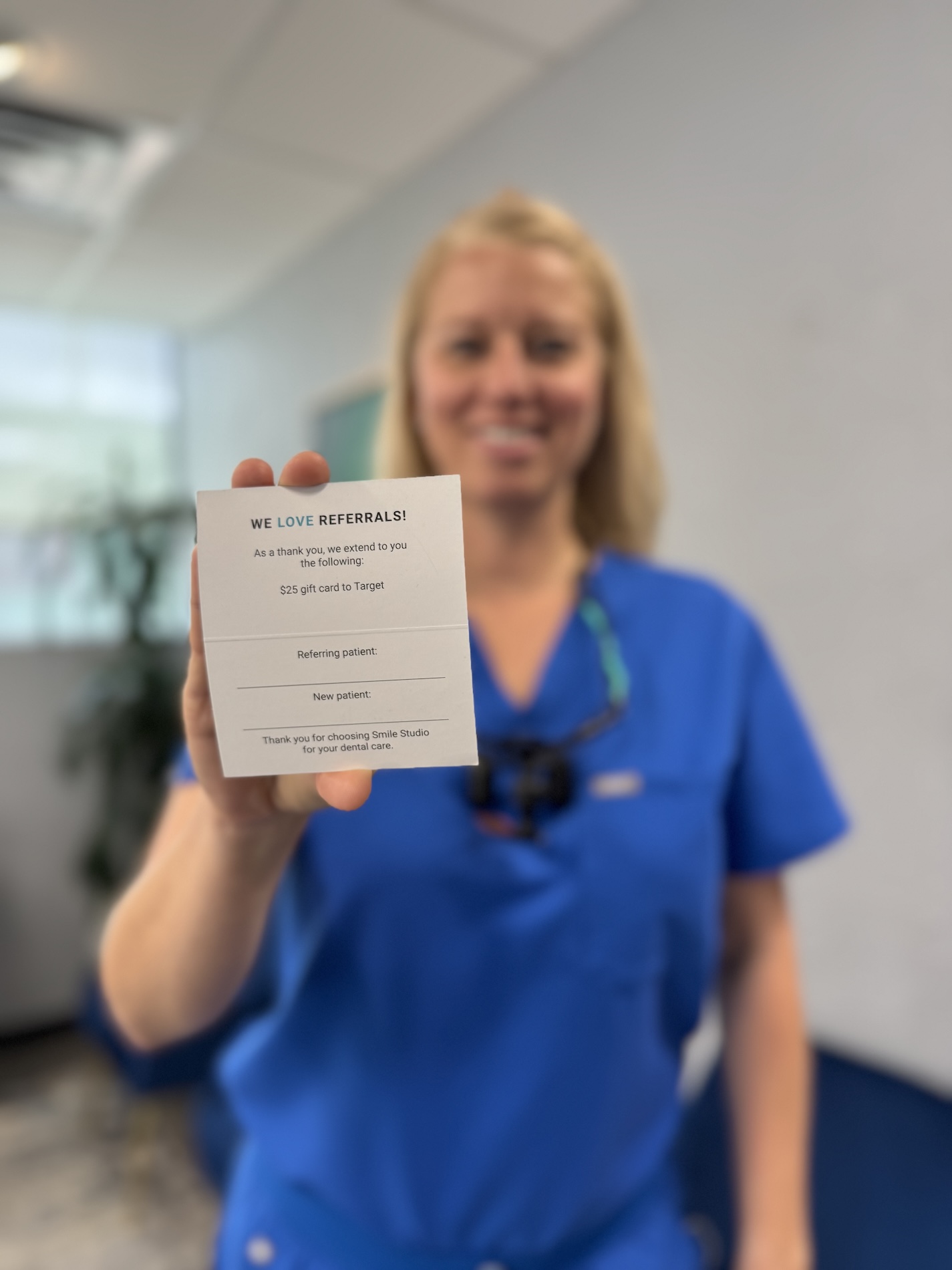 A woman in a blue scrubs stands holding up a card with text on it, likely in an office setting.