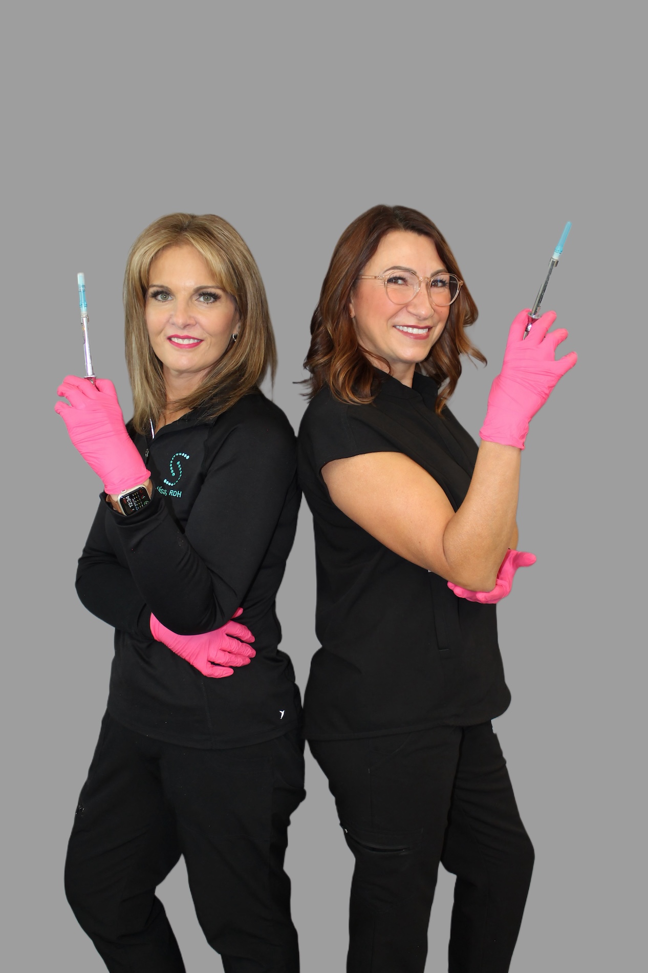 Two women posing with blue gloves, each holding a syringe, against a white background.