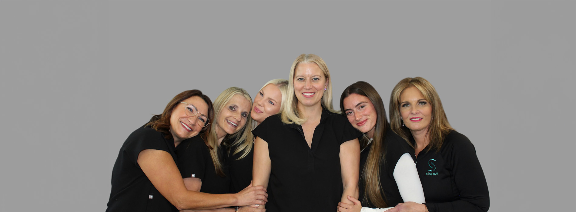 The image shows a group of five people posing together for a photo they are smiling and appear to be in a professional setting, possibly an office or salon.