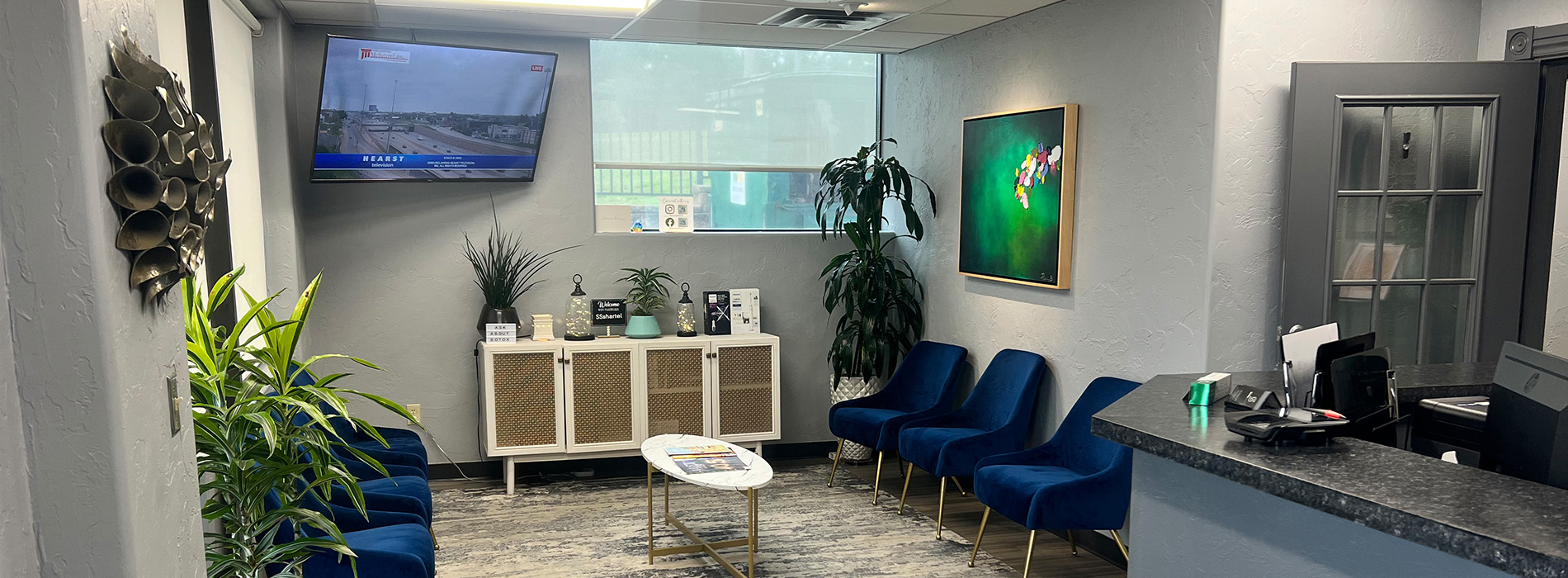 The image shows an interior space that appears to be a modern office or waiting area with contemporary furnishings, including chairs, a desk, and a television monitor on the wall displaying a landscape scene.