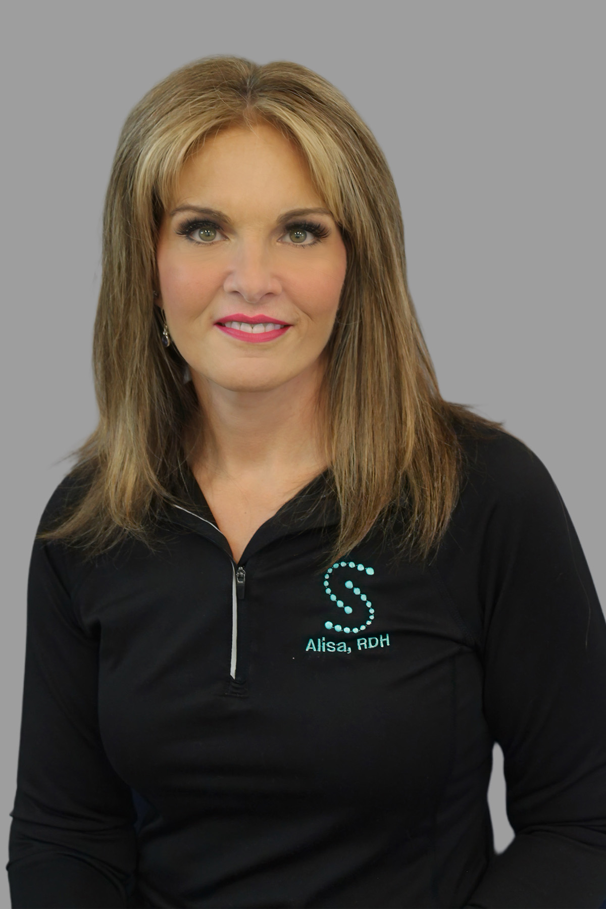 The image features a woman with blonde hair wearing a black top with a logo on the right chest area, standing against a plain background.