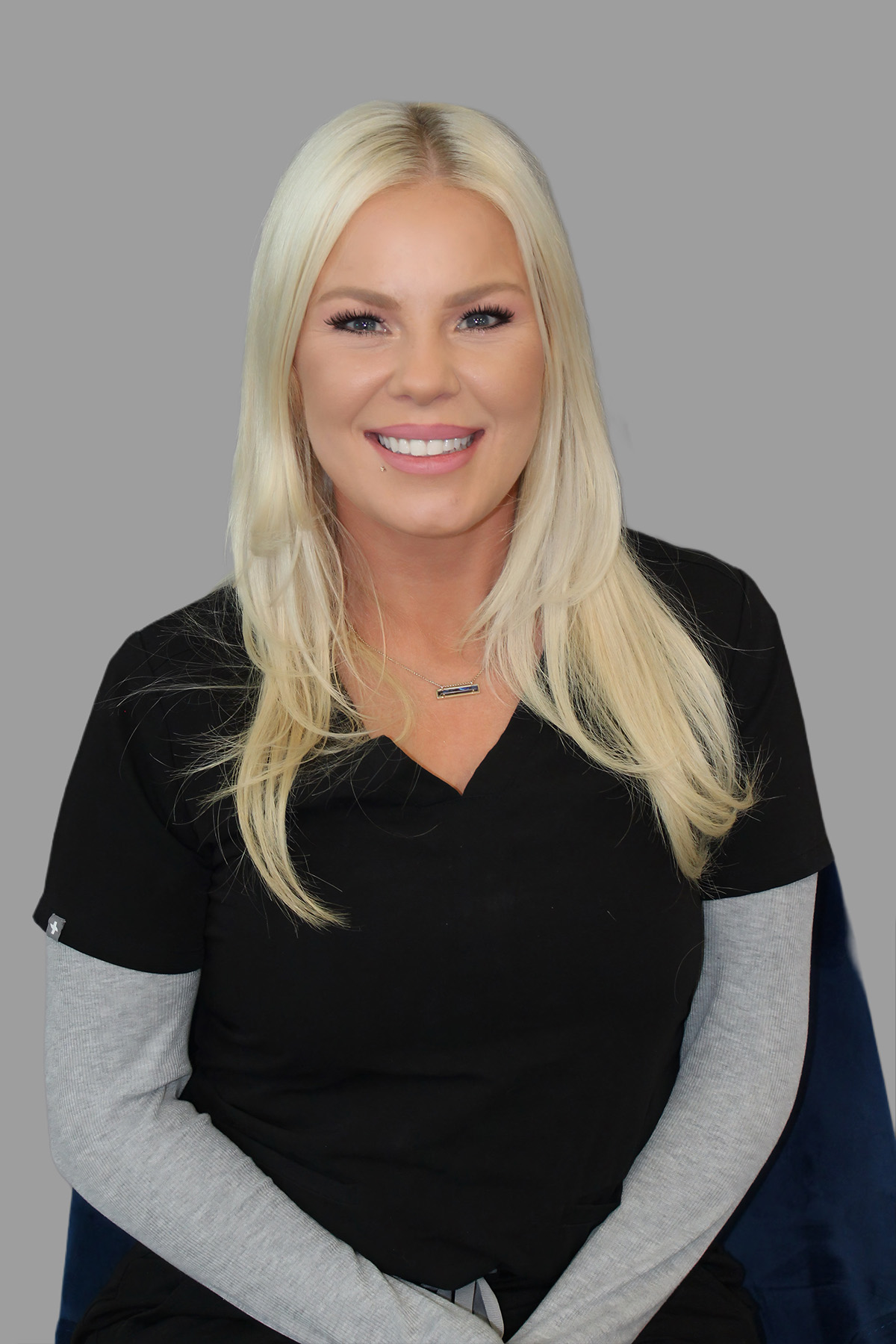 Woman wearing a black shirt and white pants with blonde hair, posing for a portrait.