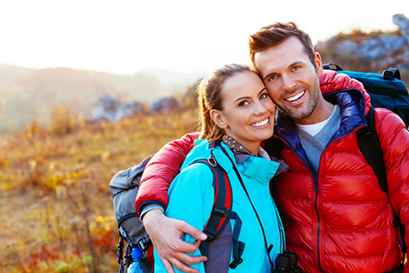 Man and woman hikers embrace outdoors, smiling at camera.
