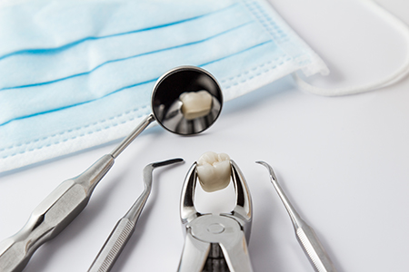 The image shows a collection of dental instruments, including a pair of scissors and a scaler, with a focus on a toothbrush being filled with toothpaste, all set against a white background with blue surgical drapes in the bottom left corner.